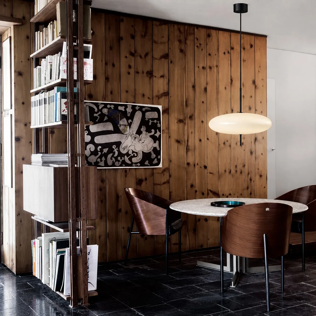 White elliptical pendant above a round table against a wood wall
