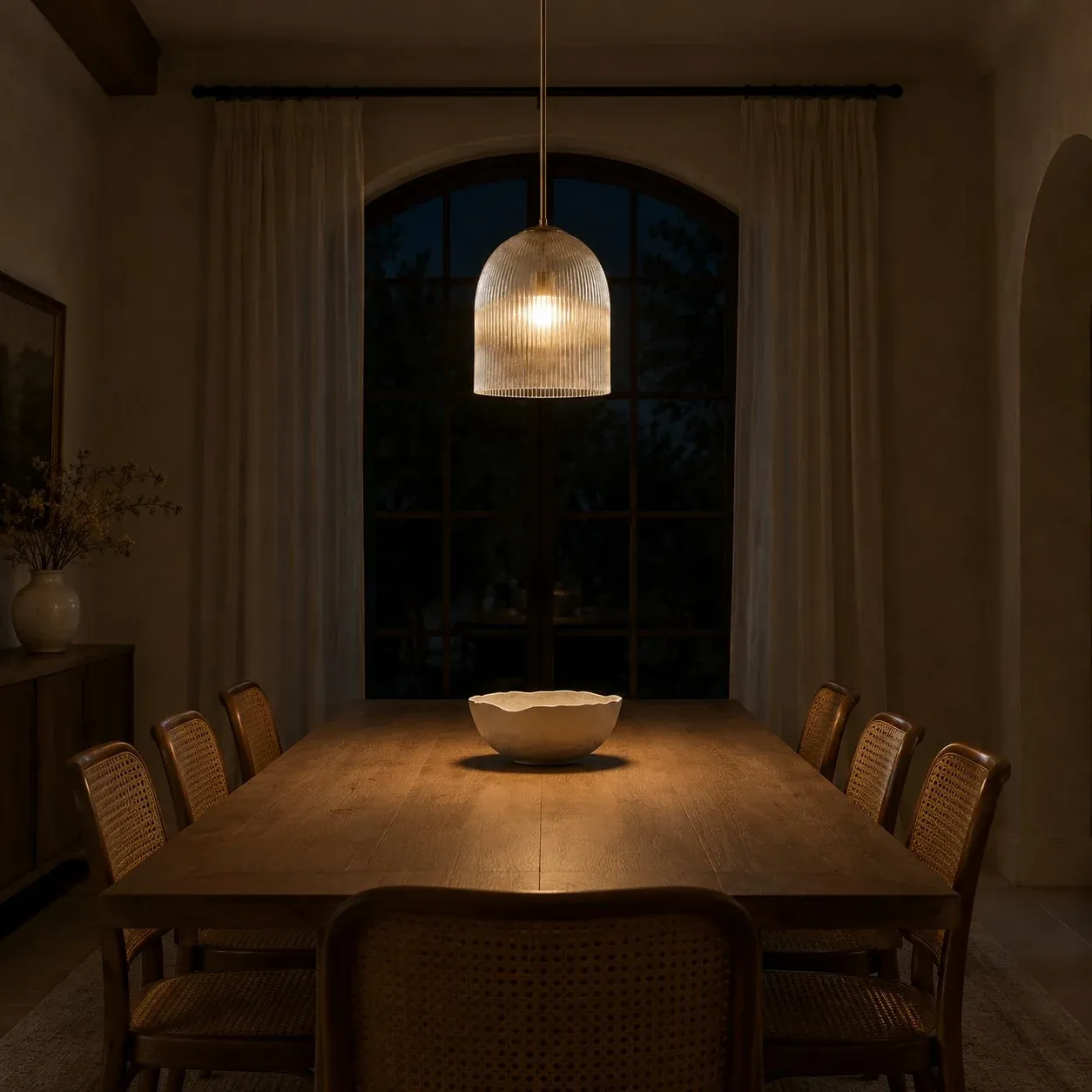 Large ribbed glass pendant lit over a dining table at night