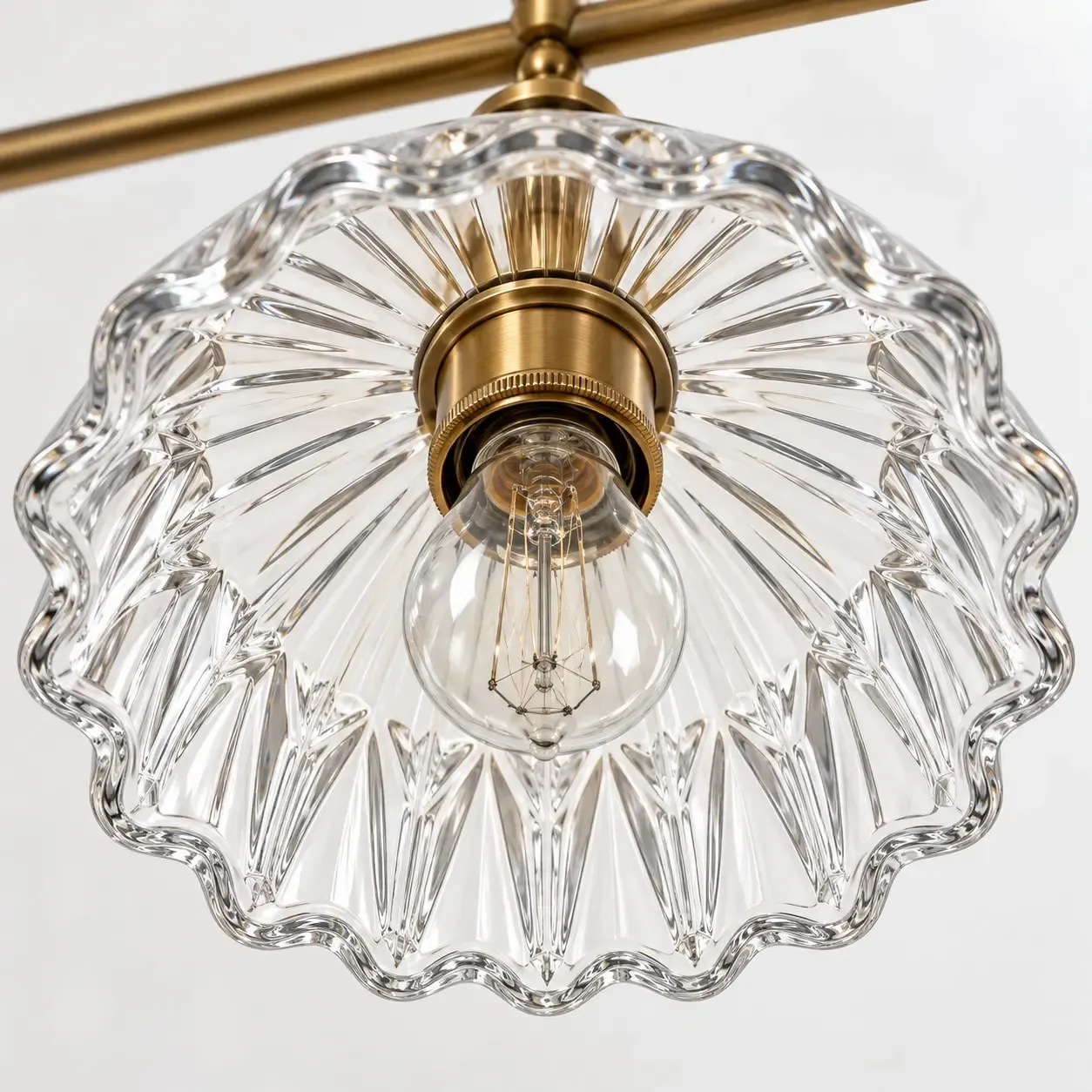 Underside of one fluted glass shade with a scalloped rim, a brass socket, and a clear globe bulb