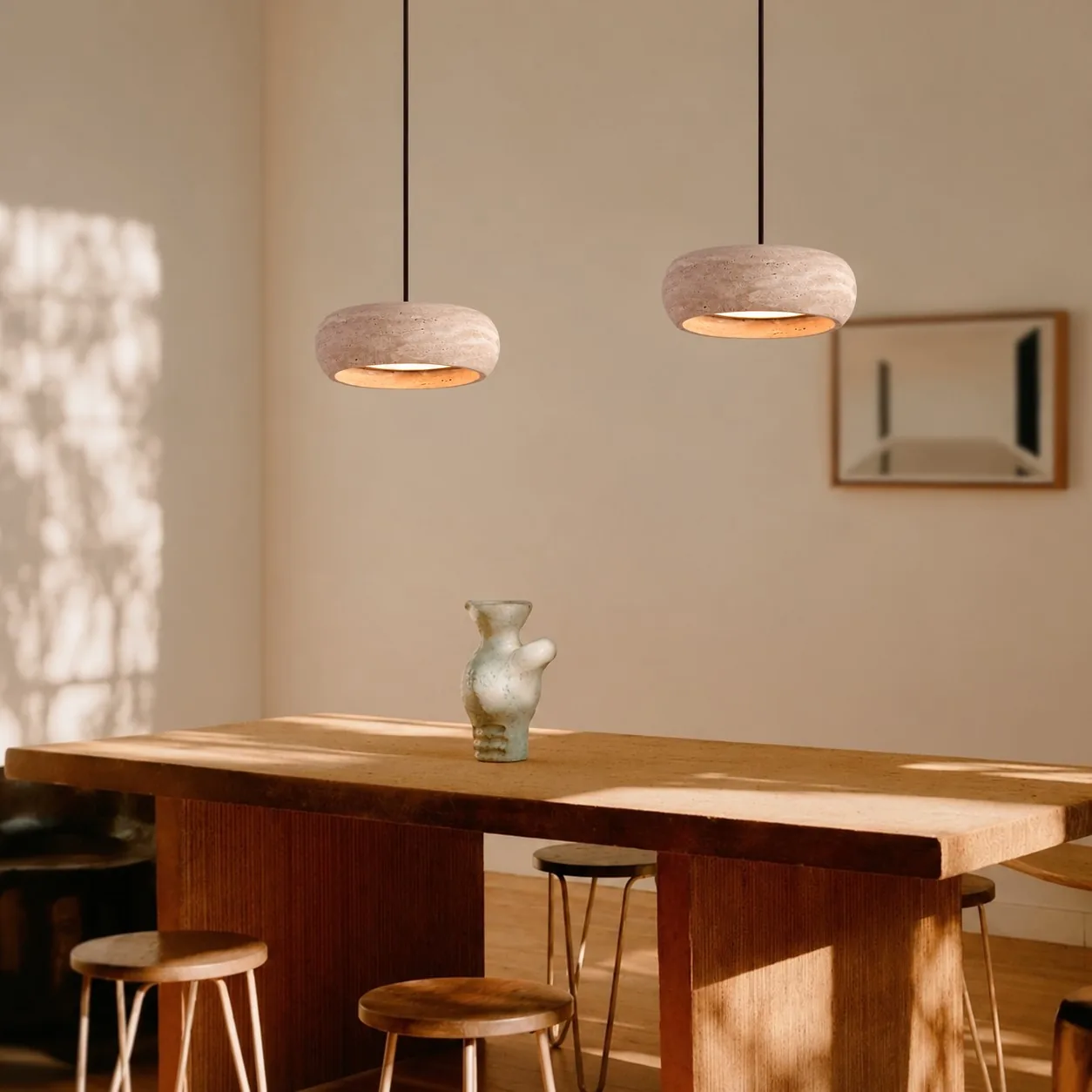 Two travertine drum pendants over a wood dining table