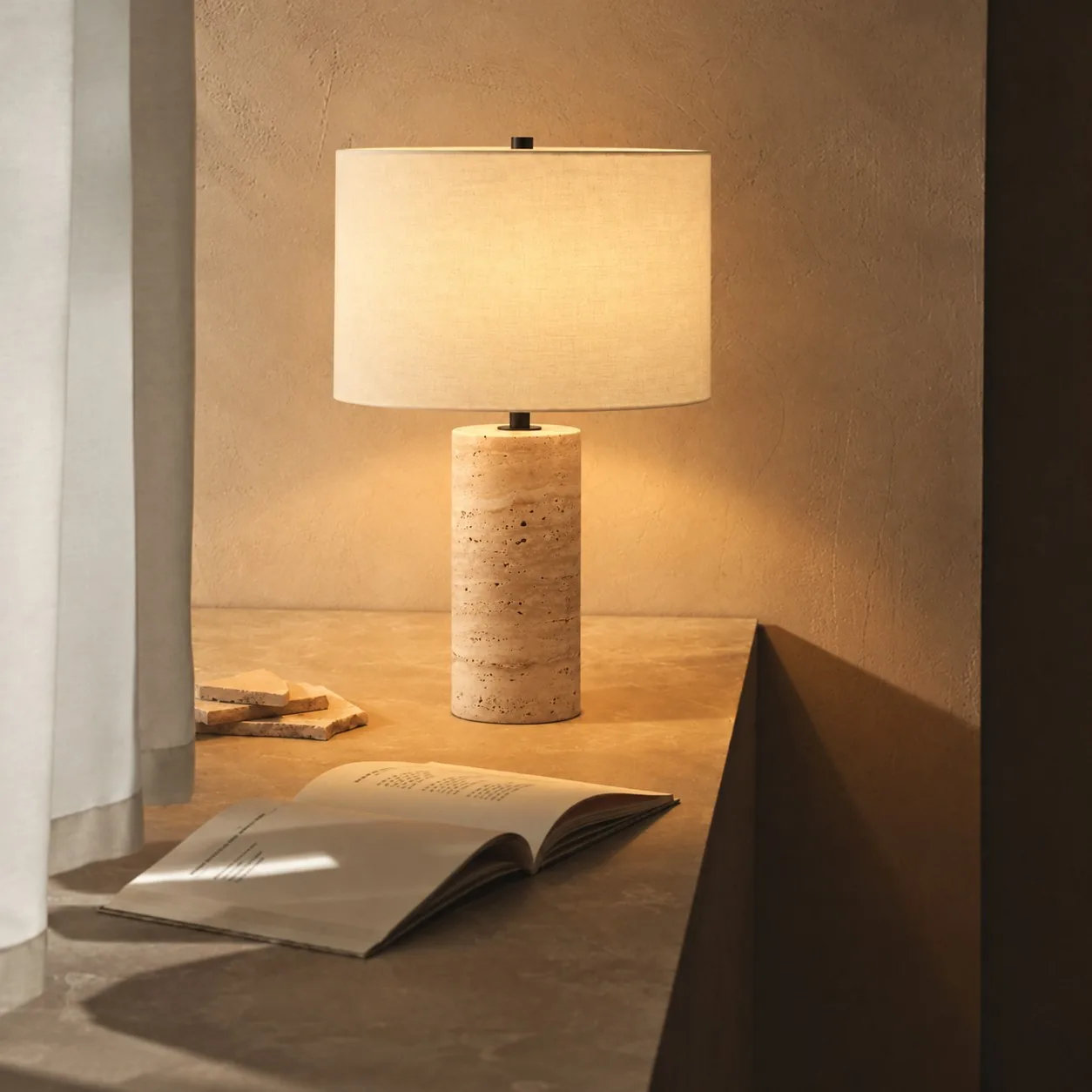 Drum Black travertine table lamp on a stone ledge