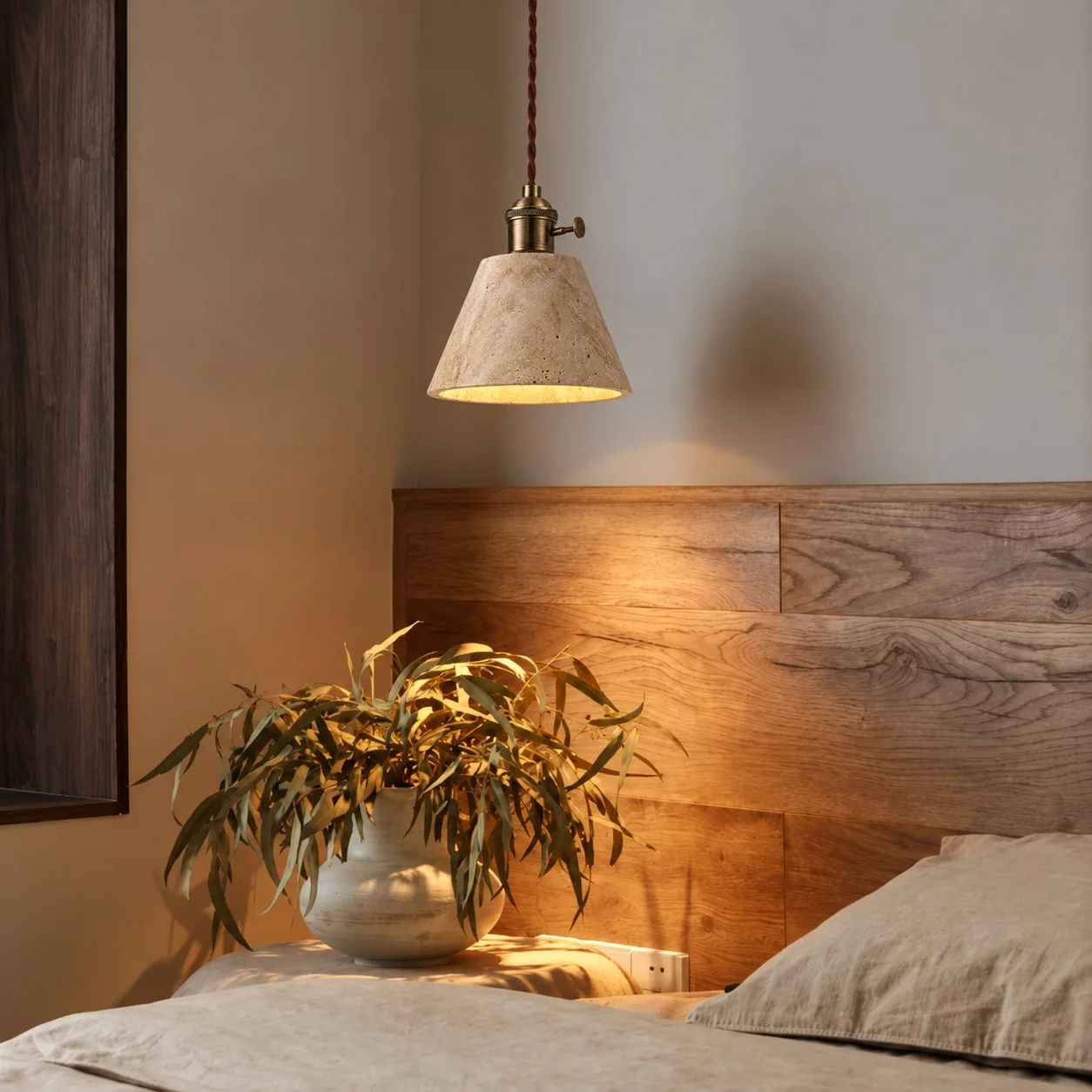 Tall cone travertine pendant above a wood headboard