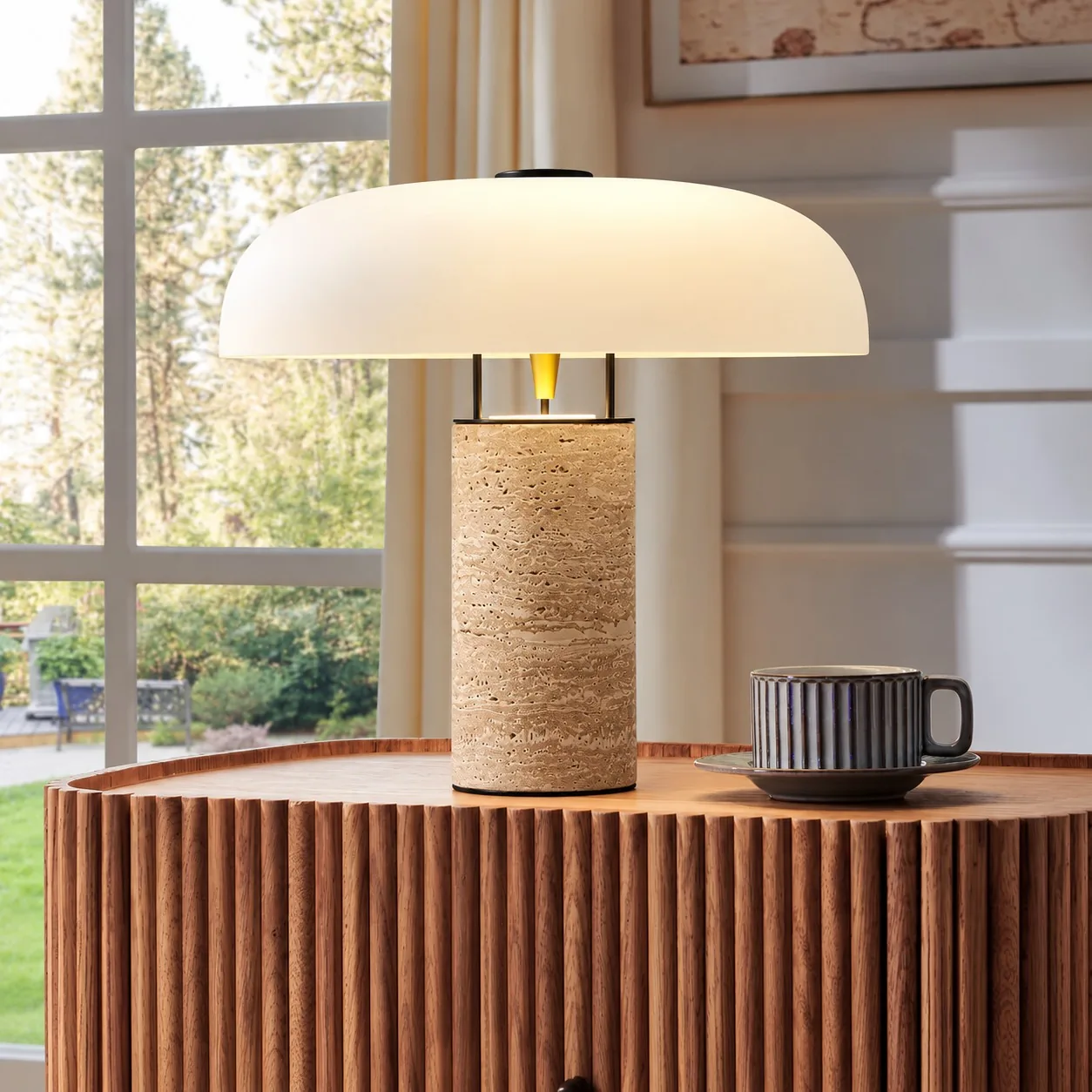 Travertine dome table lamp on a fluted wood cabinet by a window